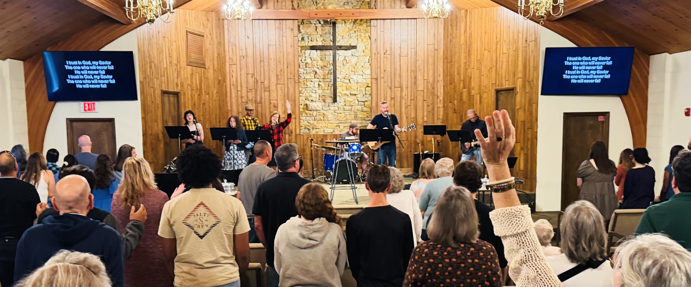 Congregation worshiping at Neighborhood Church, with the band on stage and the cross